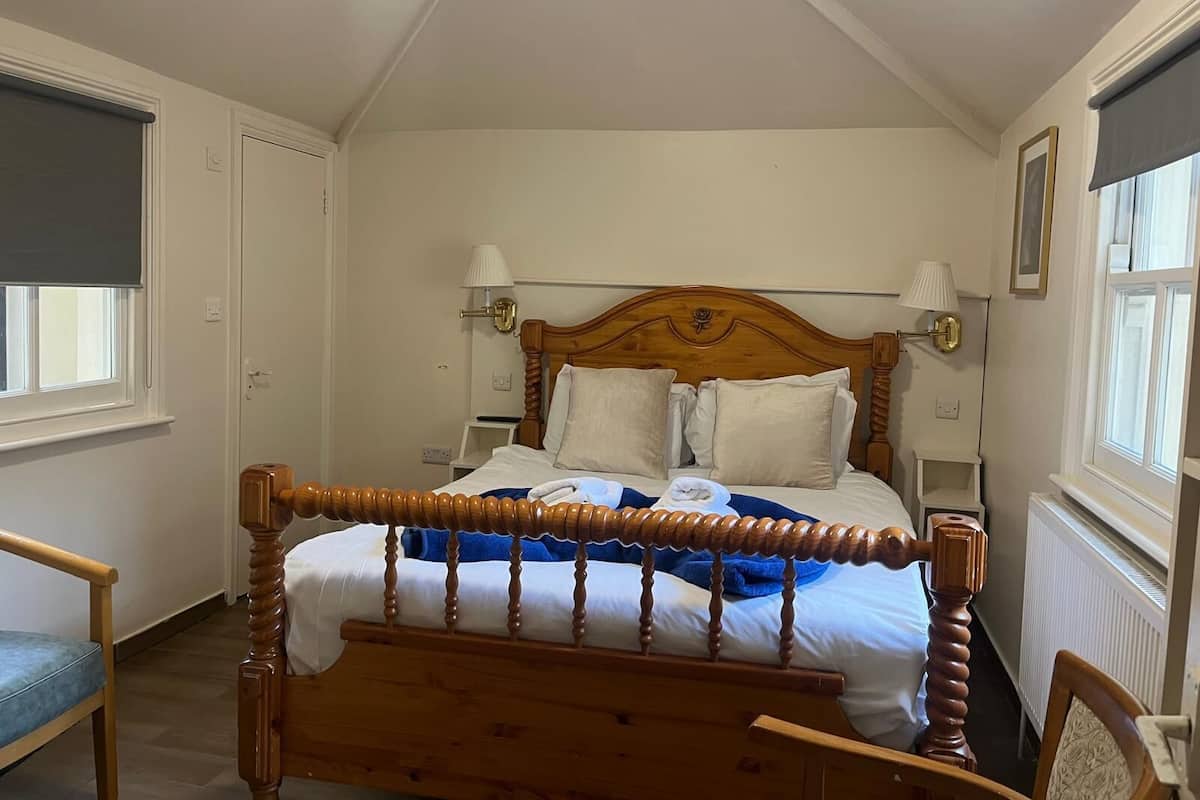 A bedroom with a wooden bed, two bedside lamps, a window with a blind, and a chair.