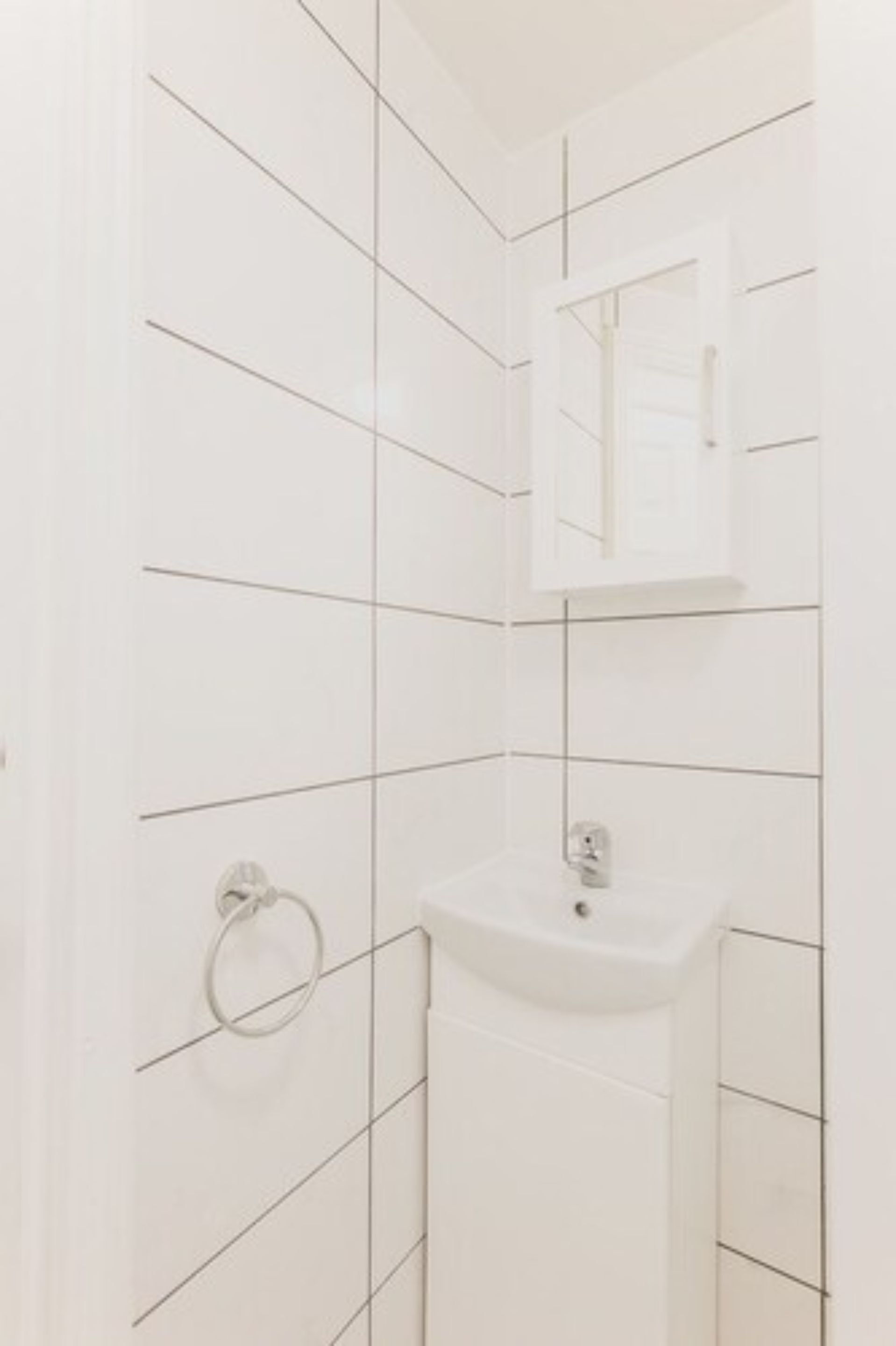 Un baño con paredes de azulejos blancos, un lavabo y un espejo.