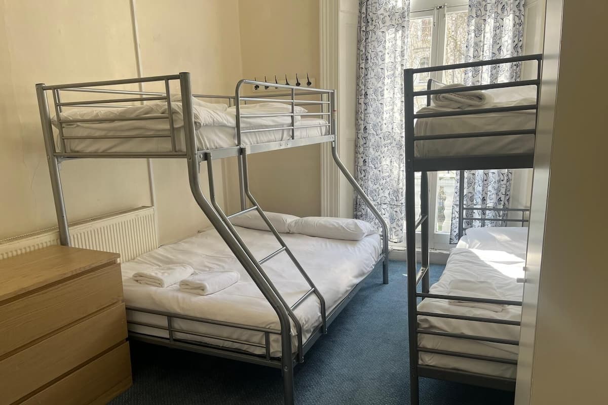A dormitory room with bunk beds, a wooden dresser, and a radiator.