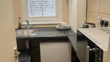 A compact kitchen with a window, a sink, a small refrigerator, and a microwave.