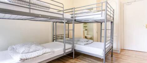 Ein Zimmer mit drei Etagenbetten, Holzboden und einer weißen Tür.