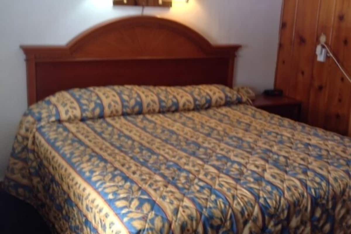 A bedroom with a wooden headboard, a patterned bedspread, and two wall-mounted lamps.