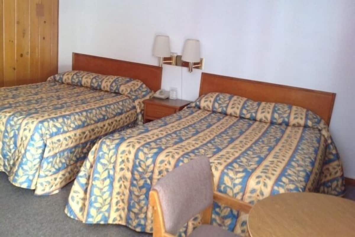 A hotel room with two beds, a wooden headboard, a nightstand with a lamp, and a small table.