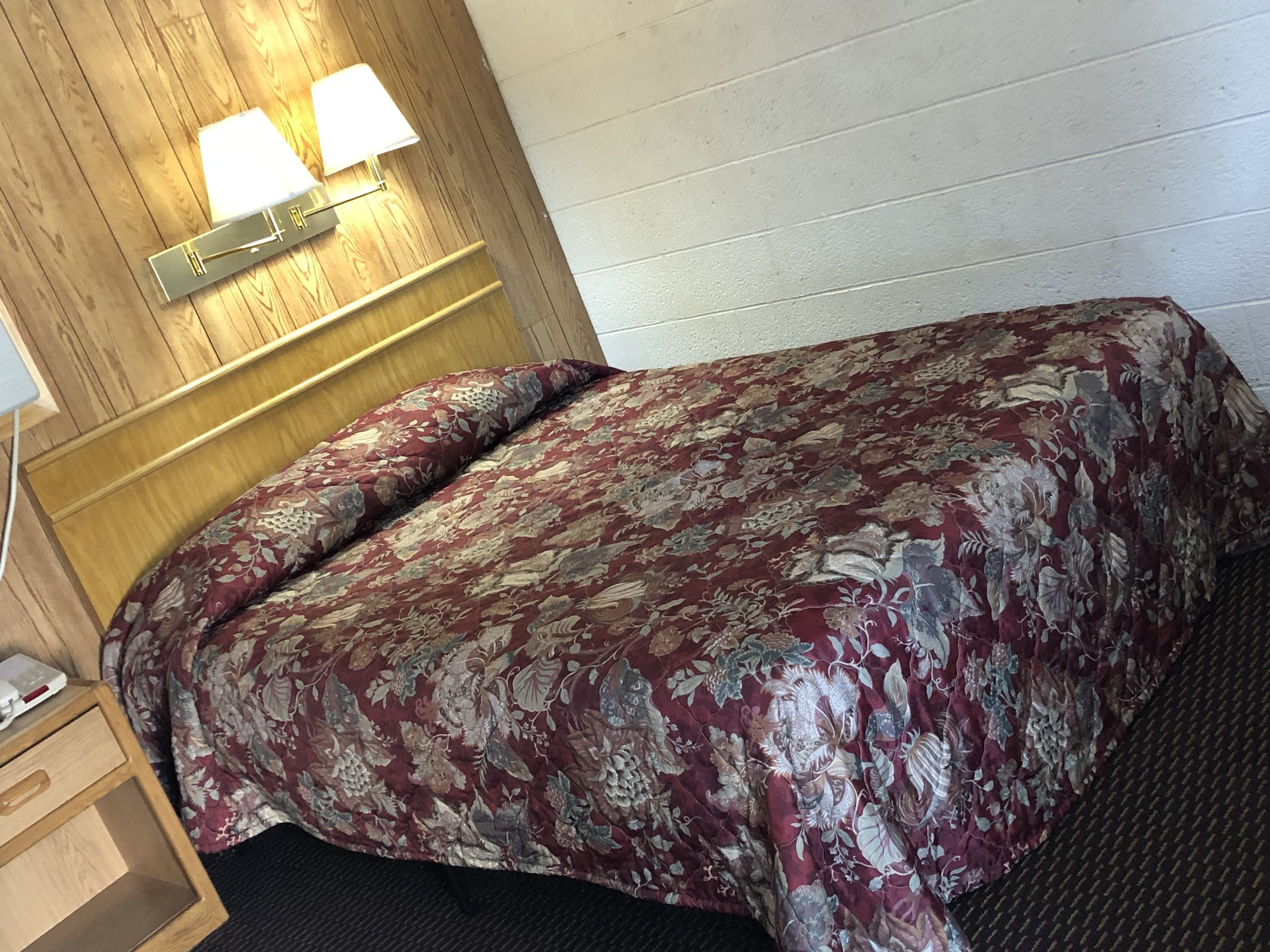 A hotel room with a wooden headboard, a floral bedspread, and two bedside lamps.
