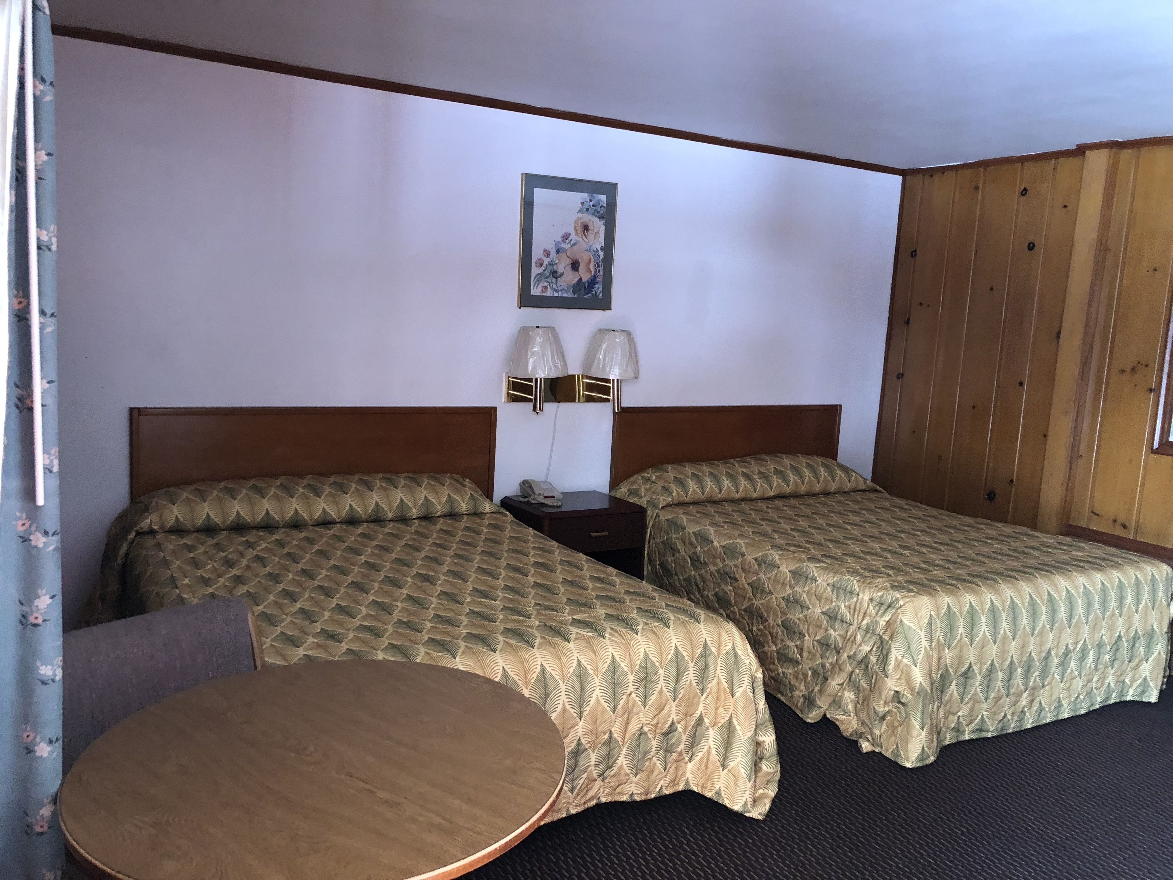 A hotel room with two beds, a small table, and a nightstand with lamps.
