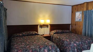 A hotel room with two beds, wooden headboards, a nightstand with a lamp, and a framed picture on the wall.