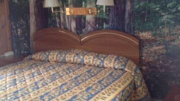 A bed with a patterned bedspread, two wall-mounted lamps, and a forest-themed wall mural.