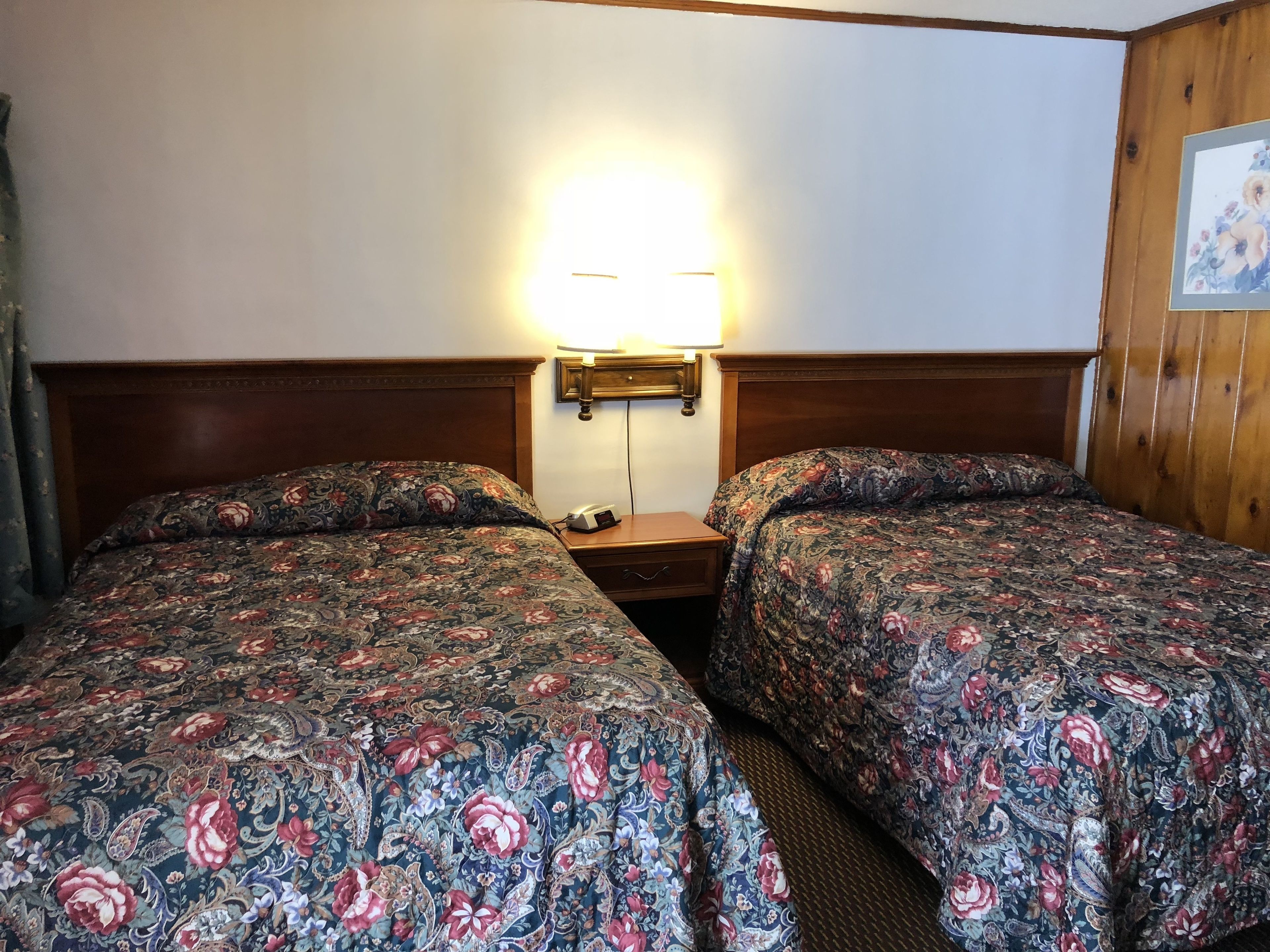 Une chambre d’hôtel avec deux lits, une table de chevet, une lampe et une tête de lit en bois.