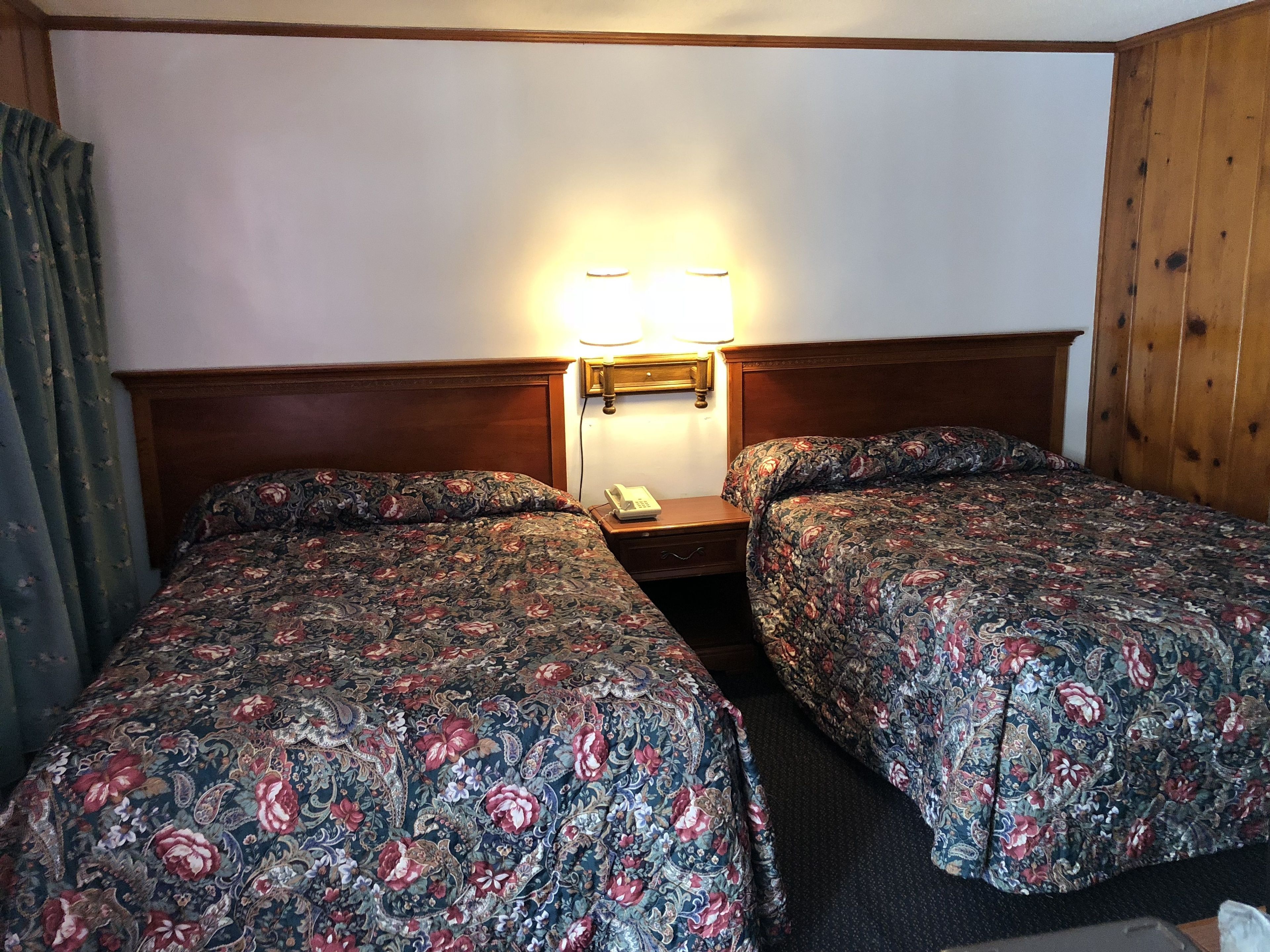 Une chambre d’hôtel avec deux lits, une table de chevet avec une lampe et une tête de lit en bois.