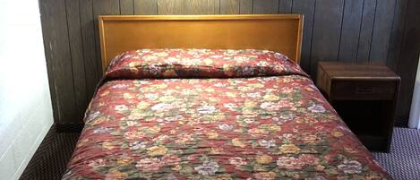 Ein Zimmer mit einem hölzernen Kopfteil, einer blumigen Tagesdecke, einem Nachttisch und einer Wandleuchte.