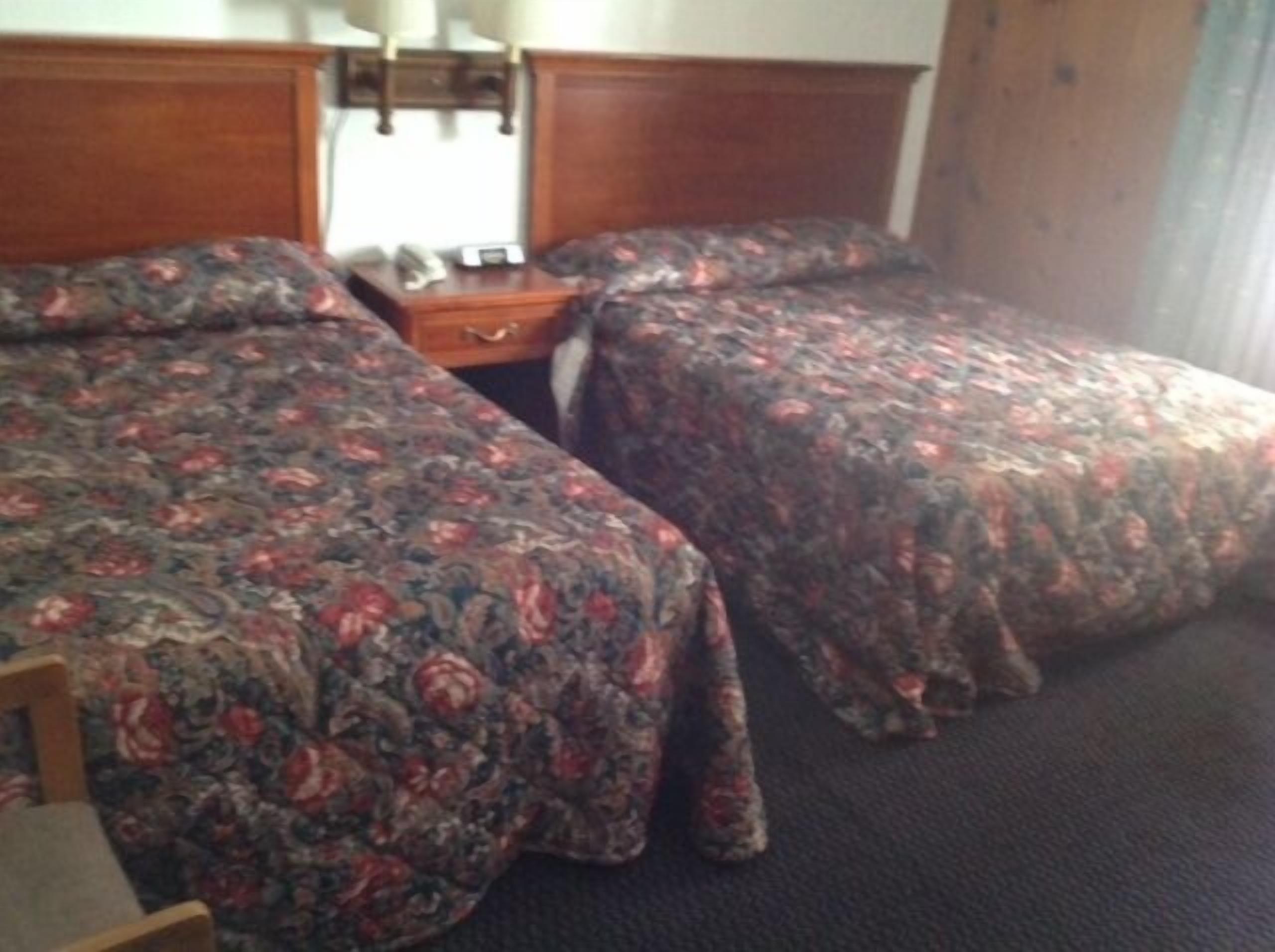 Una habitación de hotel con dos camas individuales, un cabecero de madera, una mesita de noche y una pequeña mesa.