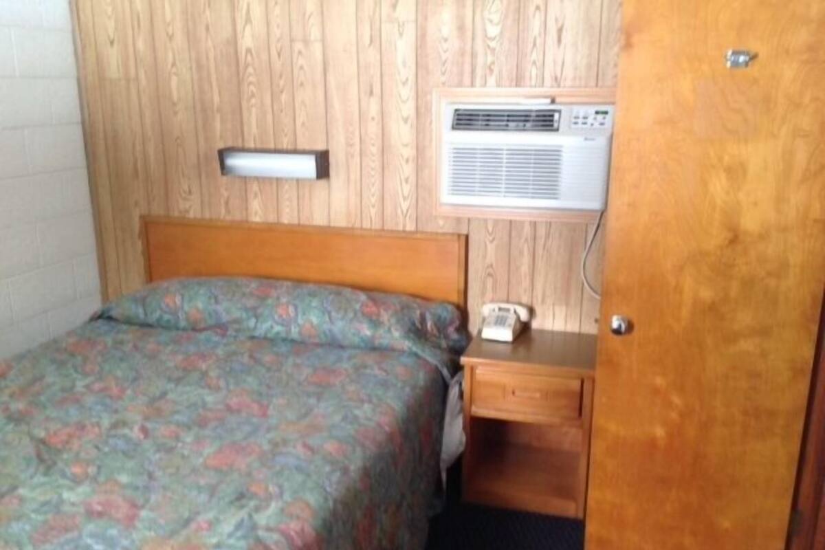 A single bed with a floral bedspread, a bedside table with a telephone, and a wall-mounted air conditioning unit.