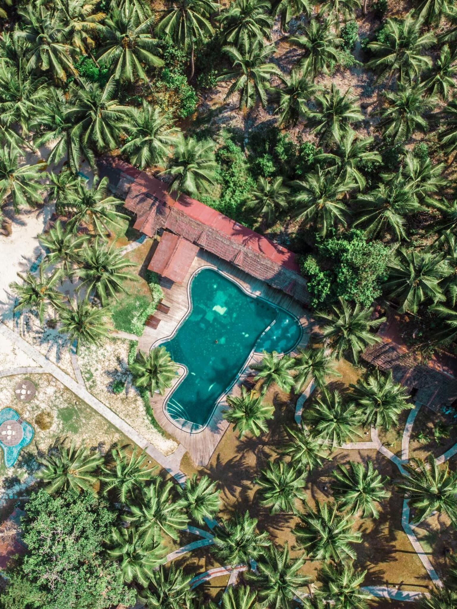 Vista aérea de un resort con piscina rodeada de palmeras.