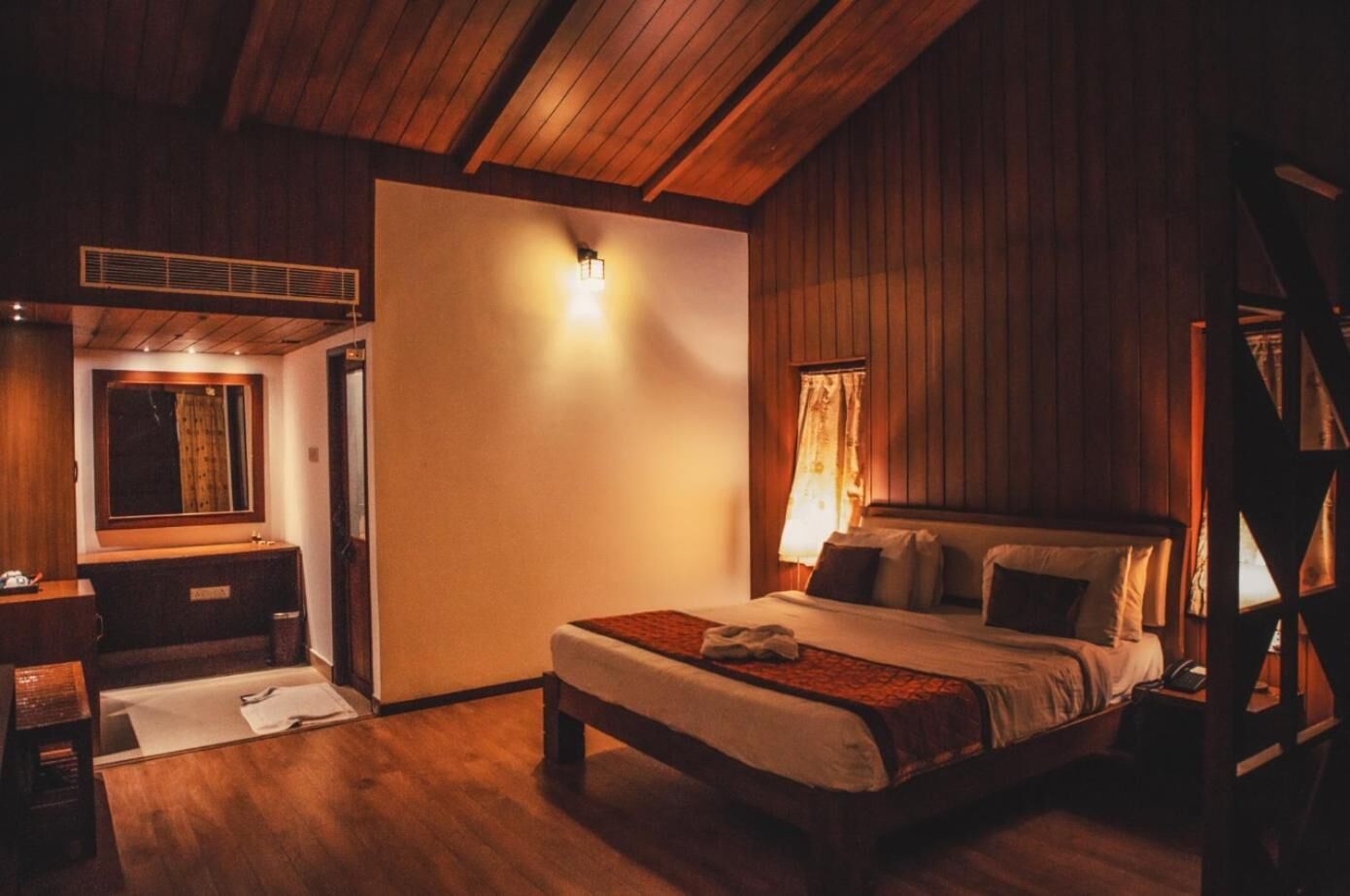 Ein gemütliches Schlafzimmer mit Holzbalkendecke, einem Bett mit Kissen, einem Nachttisch, einem Spiegel und einem Fenster mit Vorhängen.