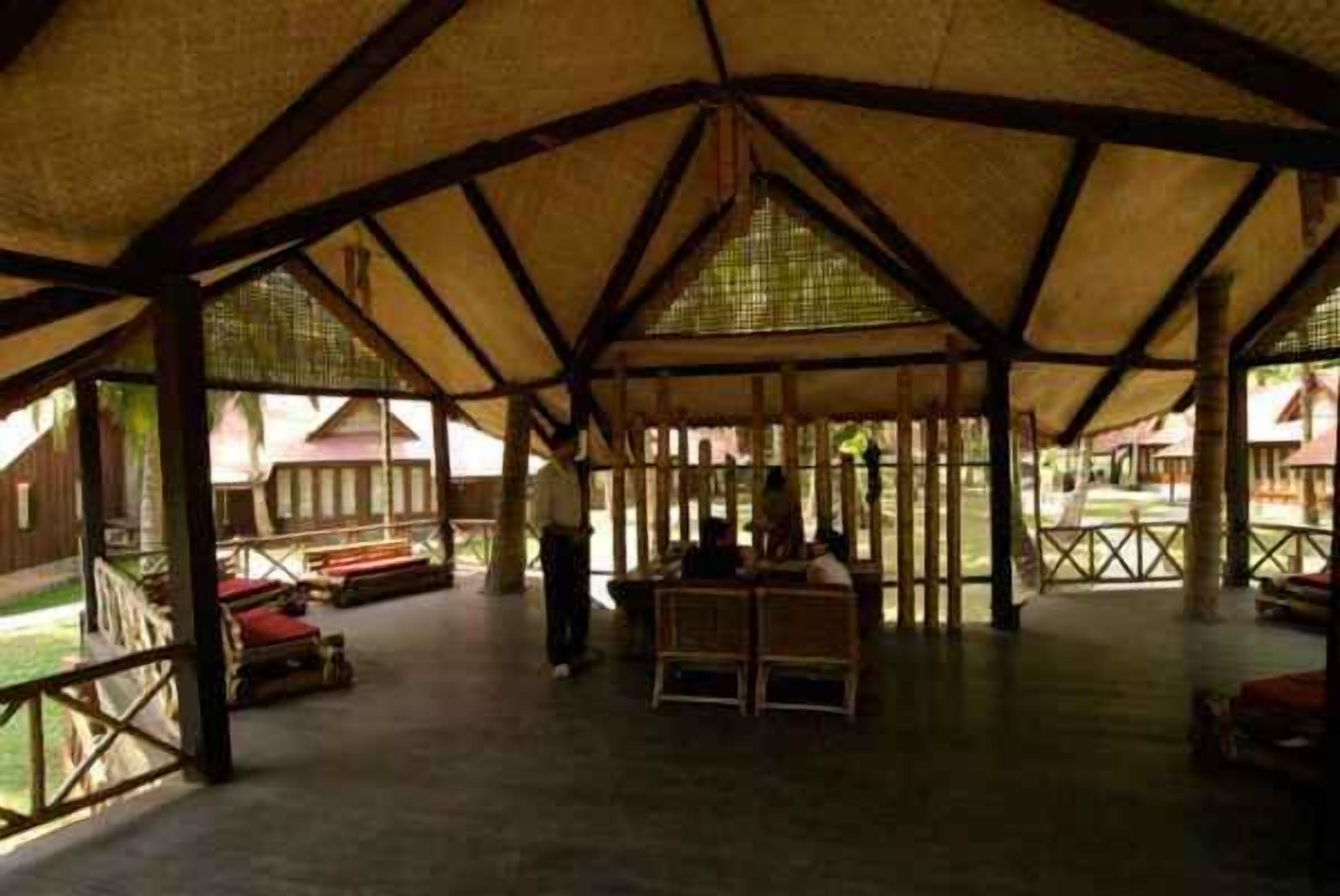 Un espacio al aire libre techado con estructura de madera, bancos y una mesa.