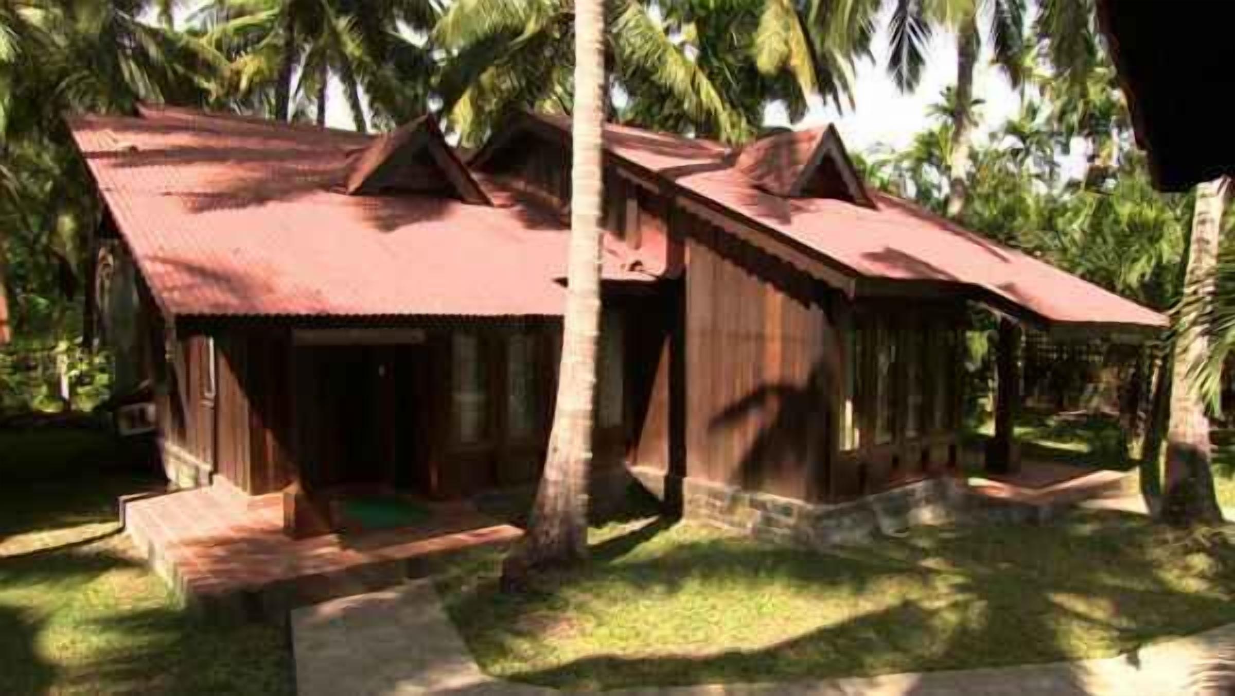 A bungalow-style building with a red roof, surrounded by palm trees.