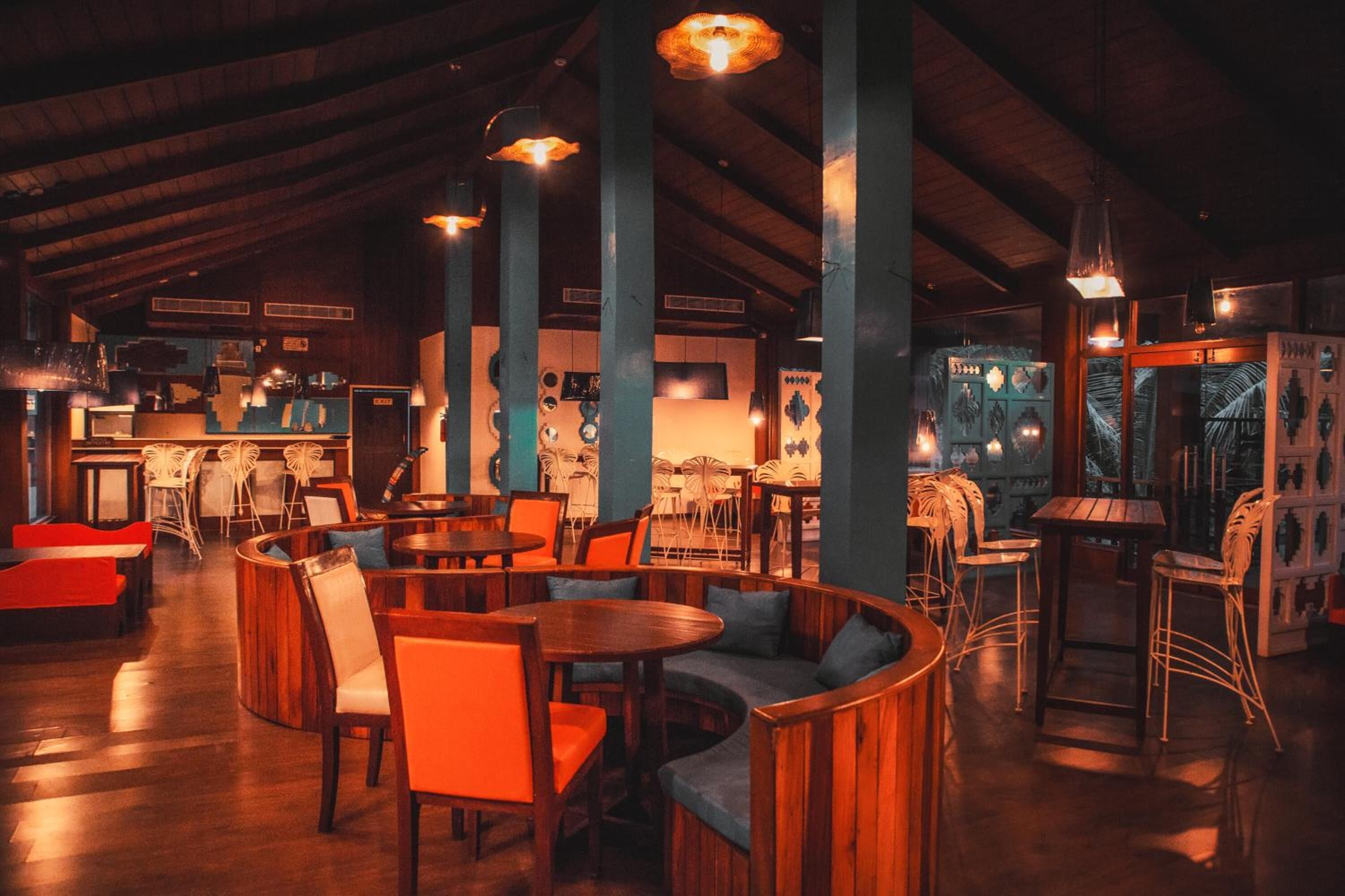 Een ruime binnenruimte met houten tafels en stoelen, een bar en decoratieve muurkunst.