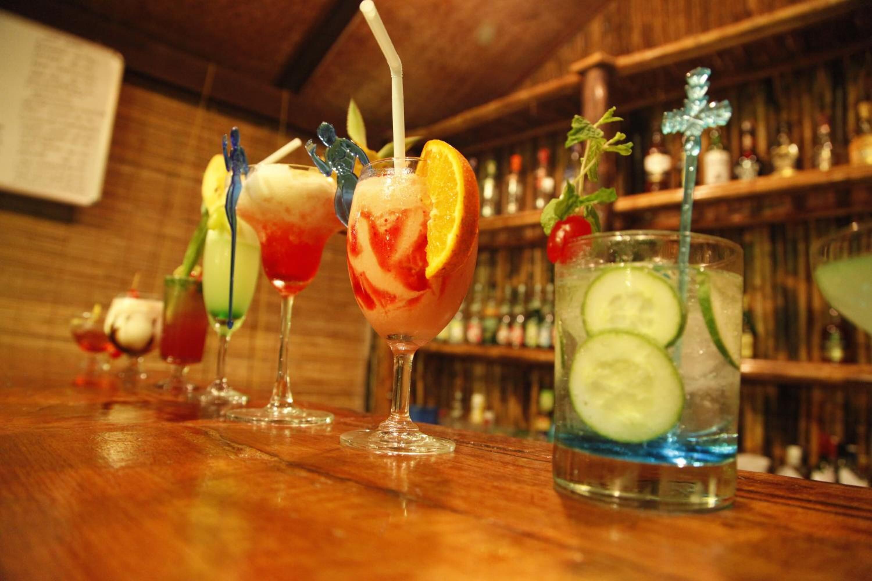 A bar with various cocktails, including a drink with a cucumber slice and mint garnish.