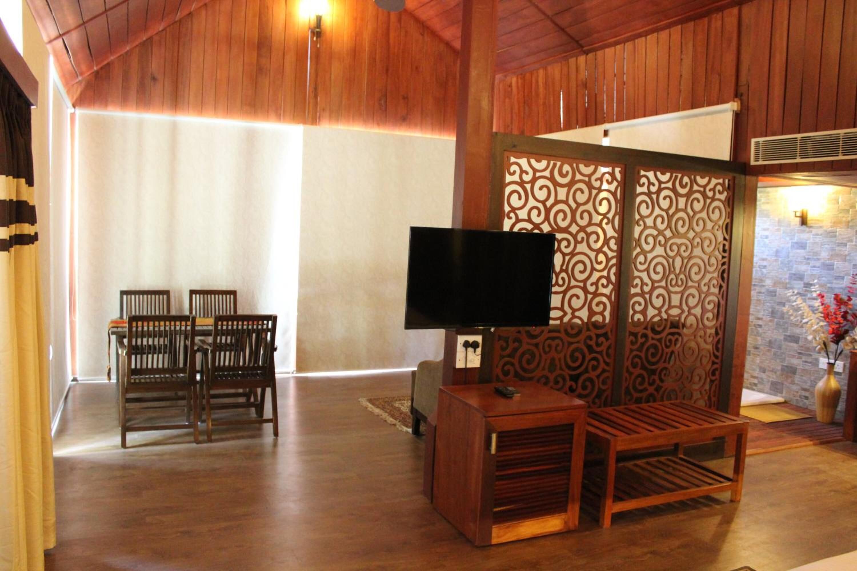 Un salón con piso de madera, un televisor, una mesa de comedor con sillas y un separador decorativo.