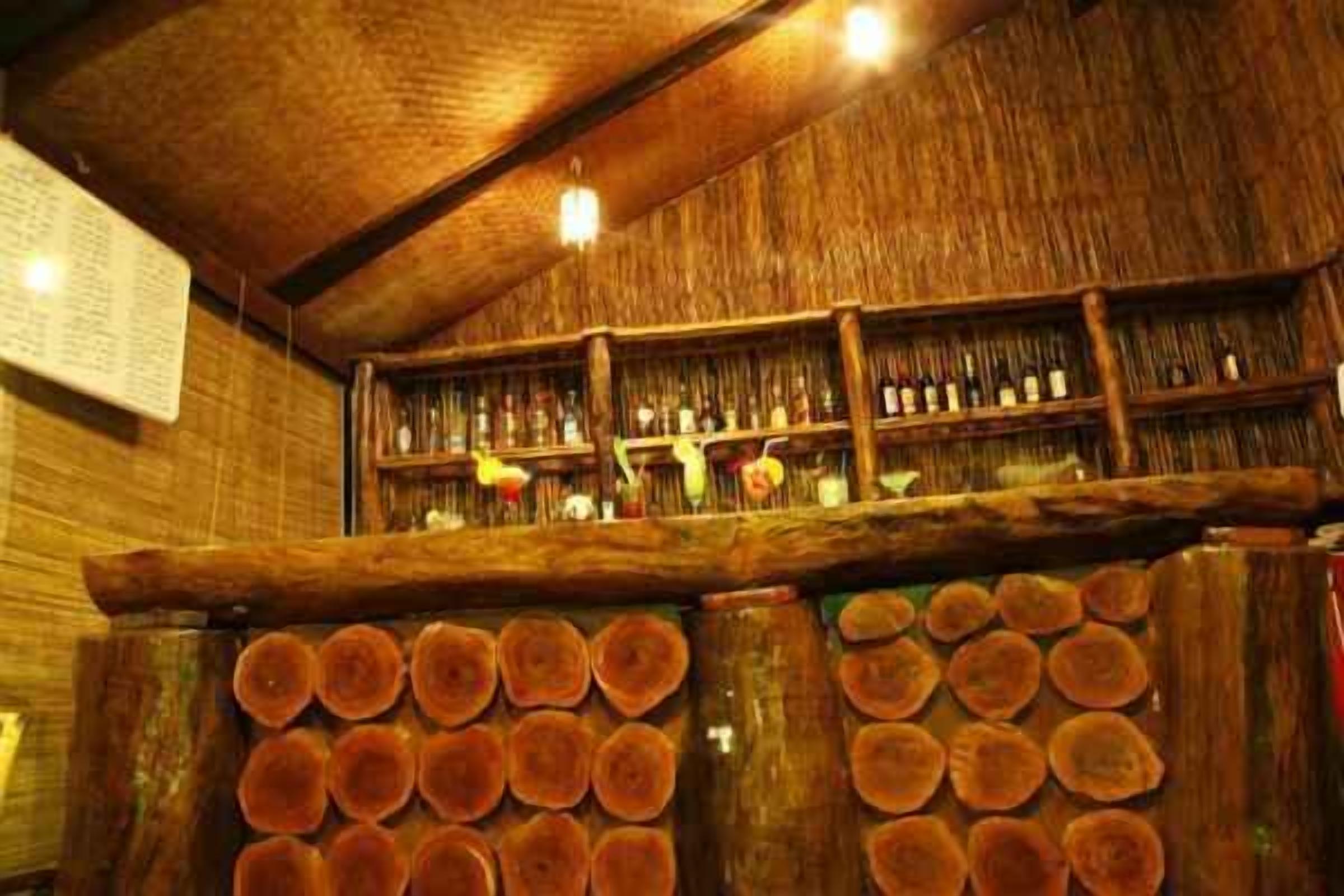 A rustic bar area with wooden shelves stocked with bottles and a stack of circular wooden logs.