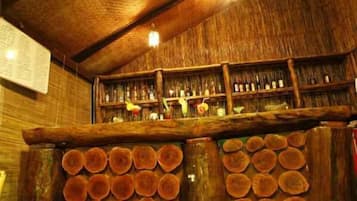 A rustic bar area with wooden shelves stocked with bottles and a stack of circular wooden logs.