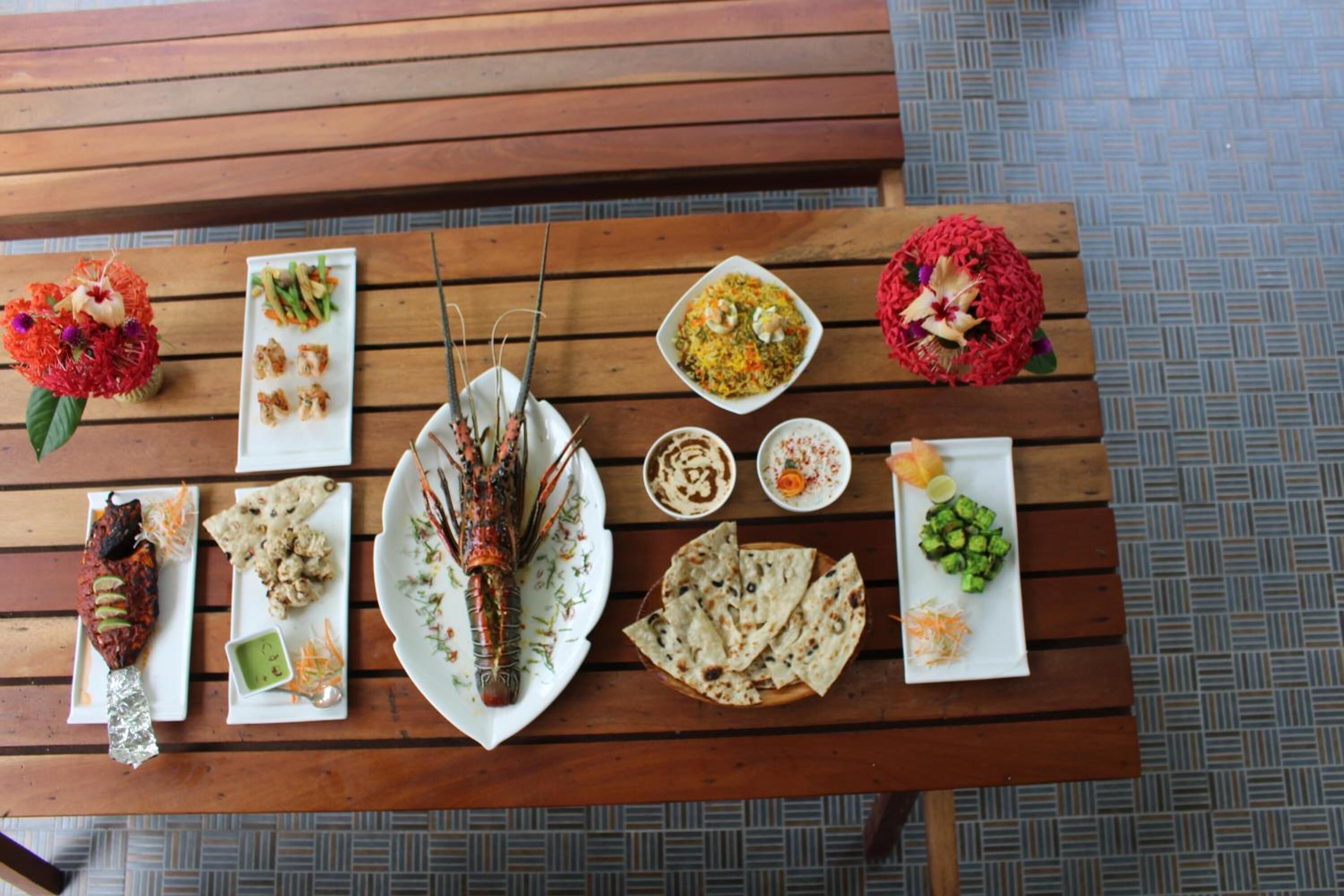 A wooden table with various dishes including grilled meat, flatbreads, and a lobster.