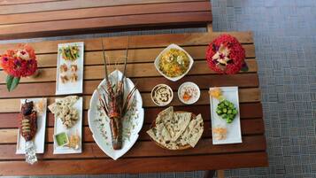 A wooden table with various dishes including grilled meat, flatbreads, and a lobster.