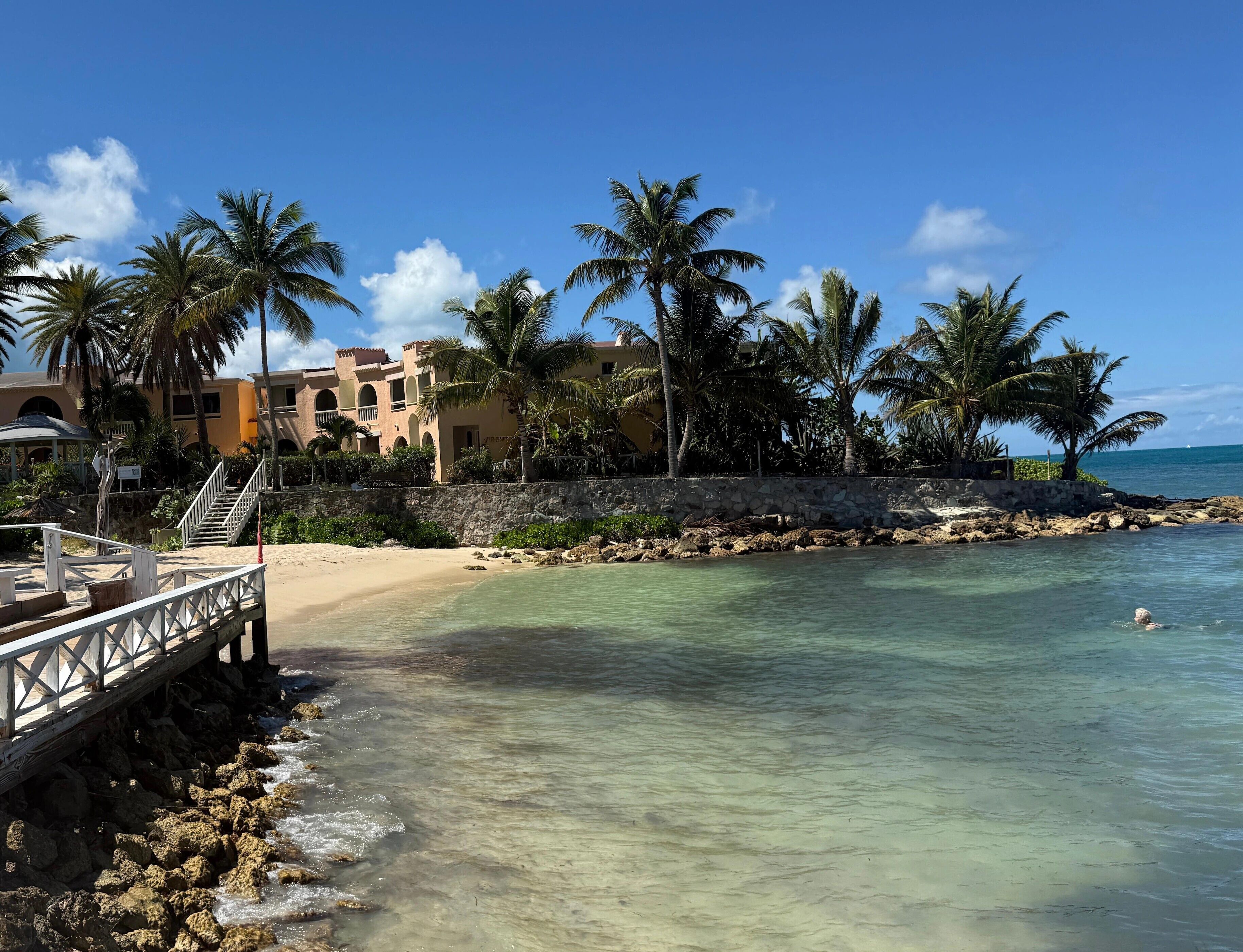 A beach with clear water, palm trees, and a building with arches.