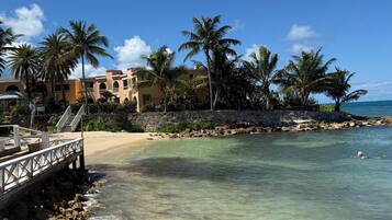 A beach with clear water, palm trees, and a building with arches.