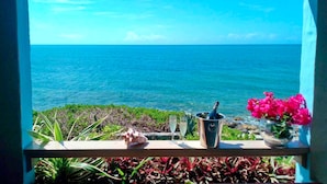 Un balcon avec vue sur l’océan, une bouteille de champagne et un vase de fleurs.