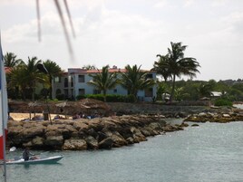Paisaje costero con un litoral rocoso, un edificio de techo rojo y palmeras.