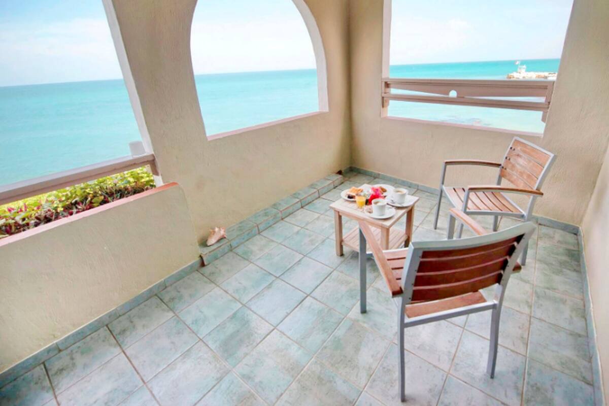 Ein Balkon mit Tisch, gedecktem Frühstück, zwei Stühlen und Blick auf das Meer.