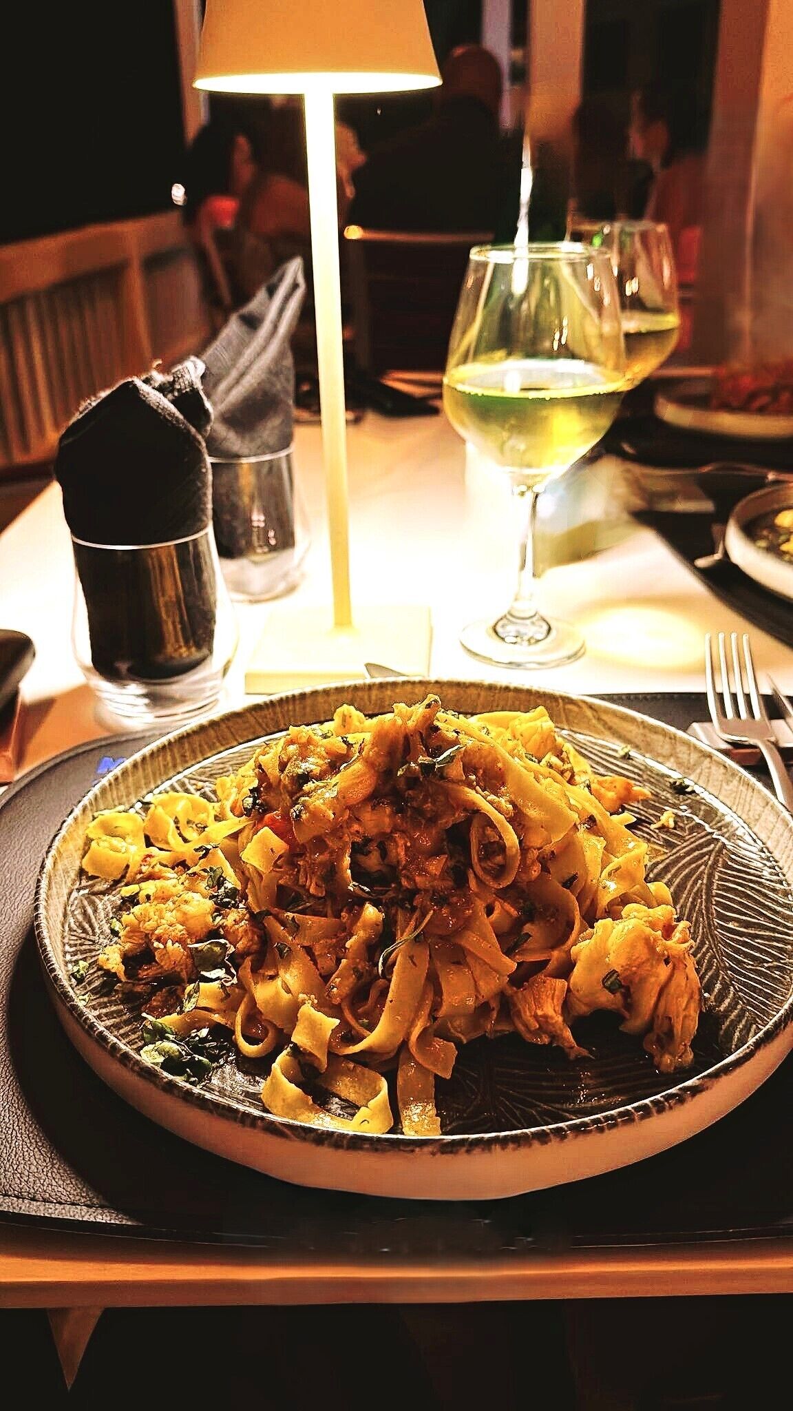 En tallerken med pasta, et glas hvidvin og et glas vand på et bord.