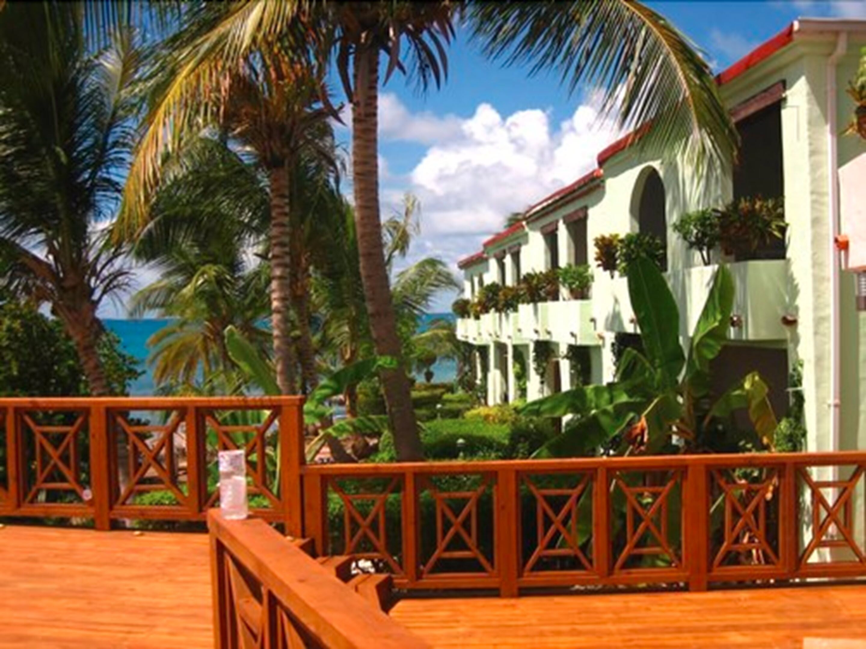 A beachfront hotel with a wooden deck, palm trees, and a view of the ocean.