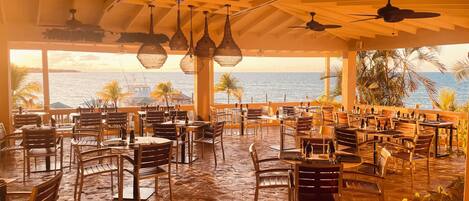 Un restaurante al aire libre con mobiliario de madera y ventiladores de techo, con vista a un cuerpo de agua.
