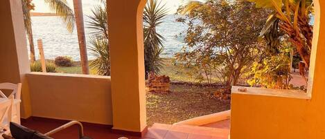 Una habitación con vistas al mar, una silla de mimbre, una mesita y una ventana con vista a palmeras y un banano.