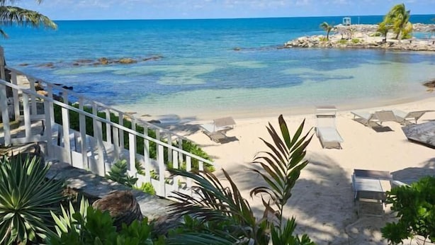 Une plage avec une vue dégagée sur l’eau, du sable blanc et des chaises longues.