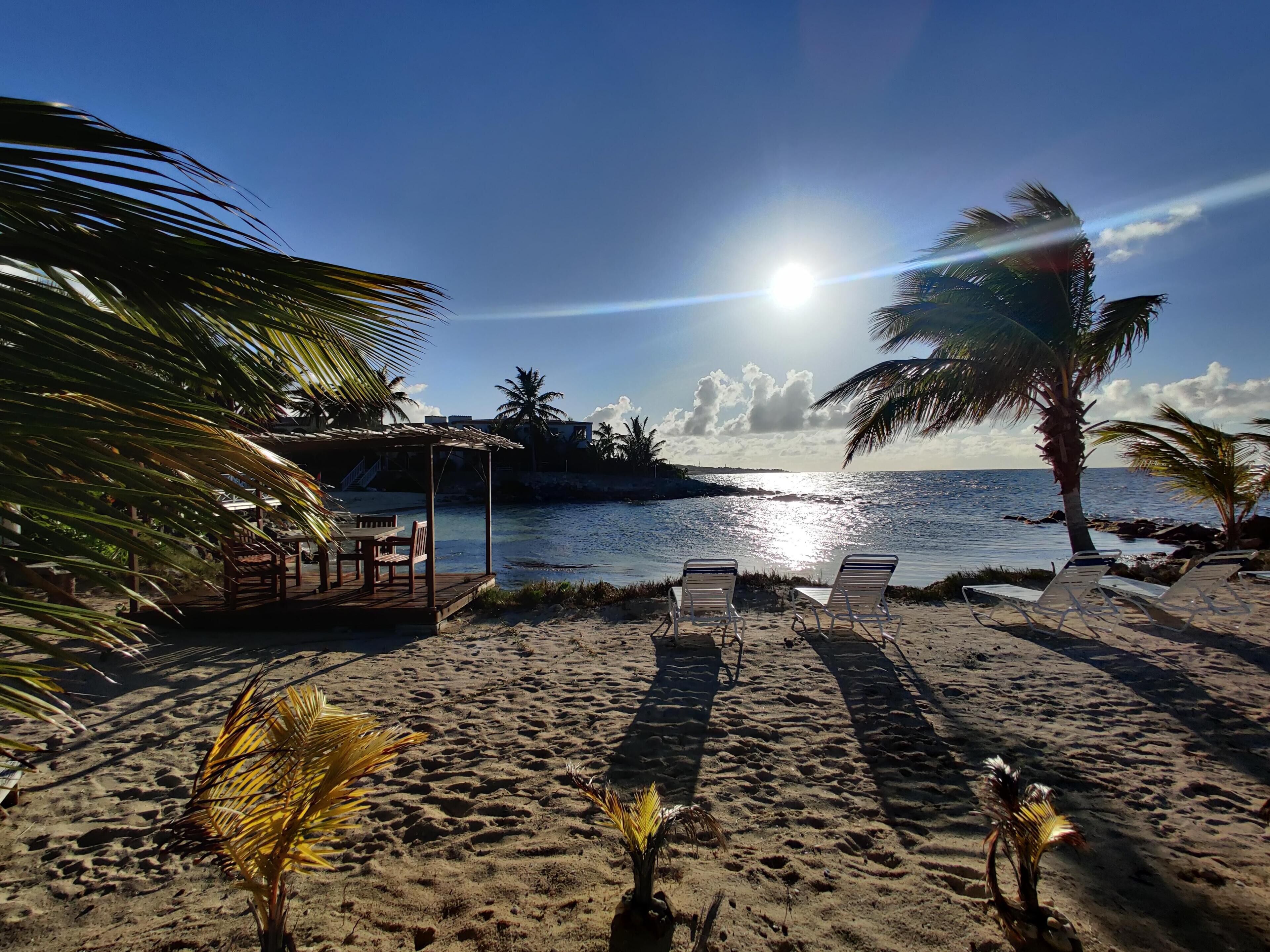 A beach with lounge chairs, a wooden structure, and palm trees.