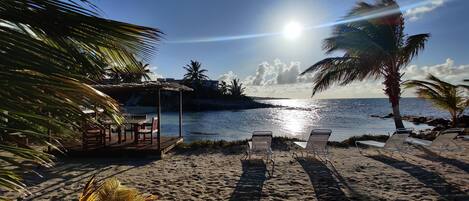 A beach with lounge chairs, a wooden structure, and palm trees.