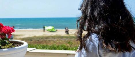 A person sitting by a window overlooking a beach with a potted plant and a cup.