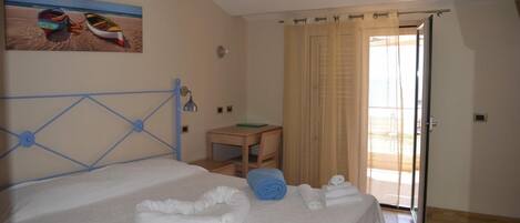 Habitación de hotel con cama, una mesita, una silla y un cuadro de barcos en la pared.