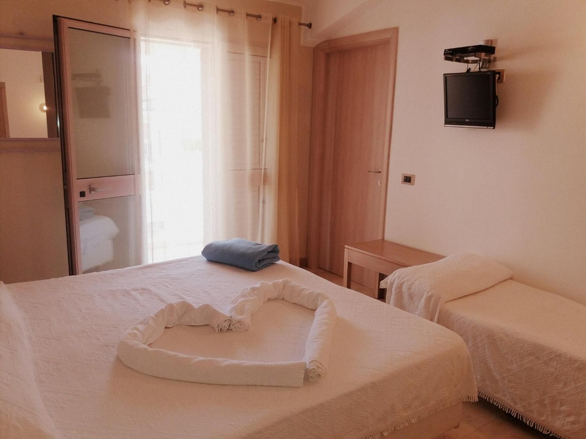 Une chambre d’hôtel avec deux lits, une petite table, un miroir et un téléviseur fixé au mur.