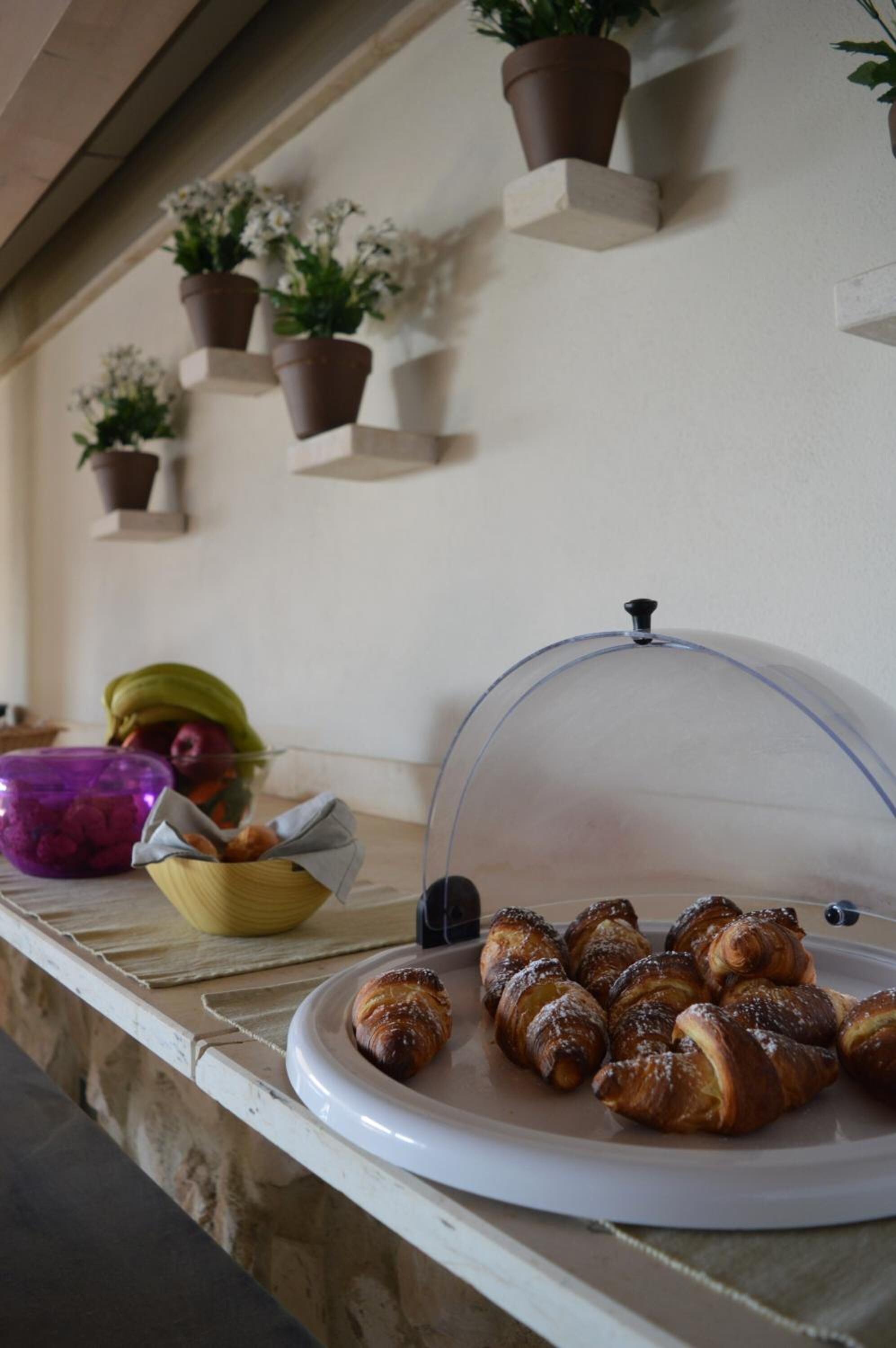 Une table de petit-déjeuner avec des viennoiseries sur une assiette, un bol de fruits et une vitrine couverte.