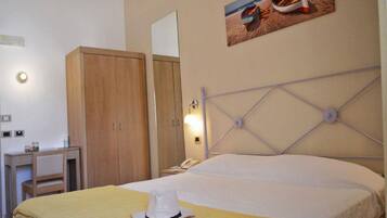 A hotel room with a bed, a wardrobe, a desk, and a painting of boats on the wall.