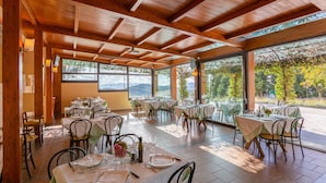 Een restaurant met meerdere tafels klaar voor diners, grote ramen met uitzicht op de omgeving, en een houten plafondconstructie.