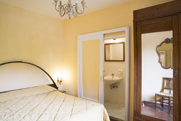 A bedroom with a bed, a chandelier, a door leading to a bathroom, and a mirror. - Villa Grassina (Pelago)
