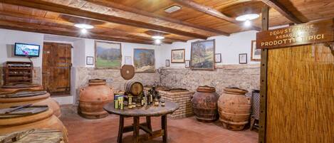 Una bodega rústica con vigas de madera, barriles de terracota y una mesa de madera con botellas.