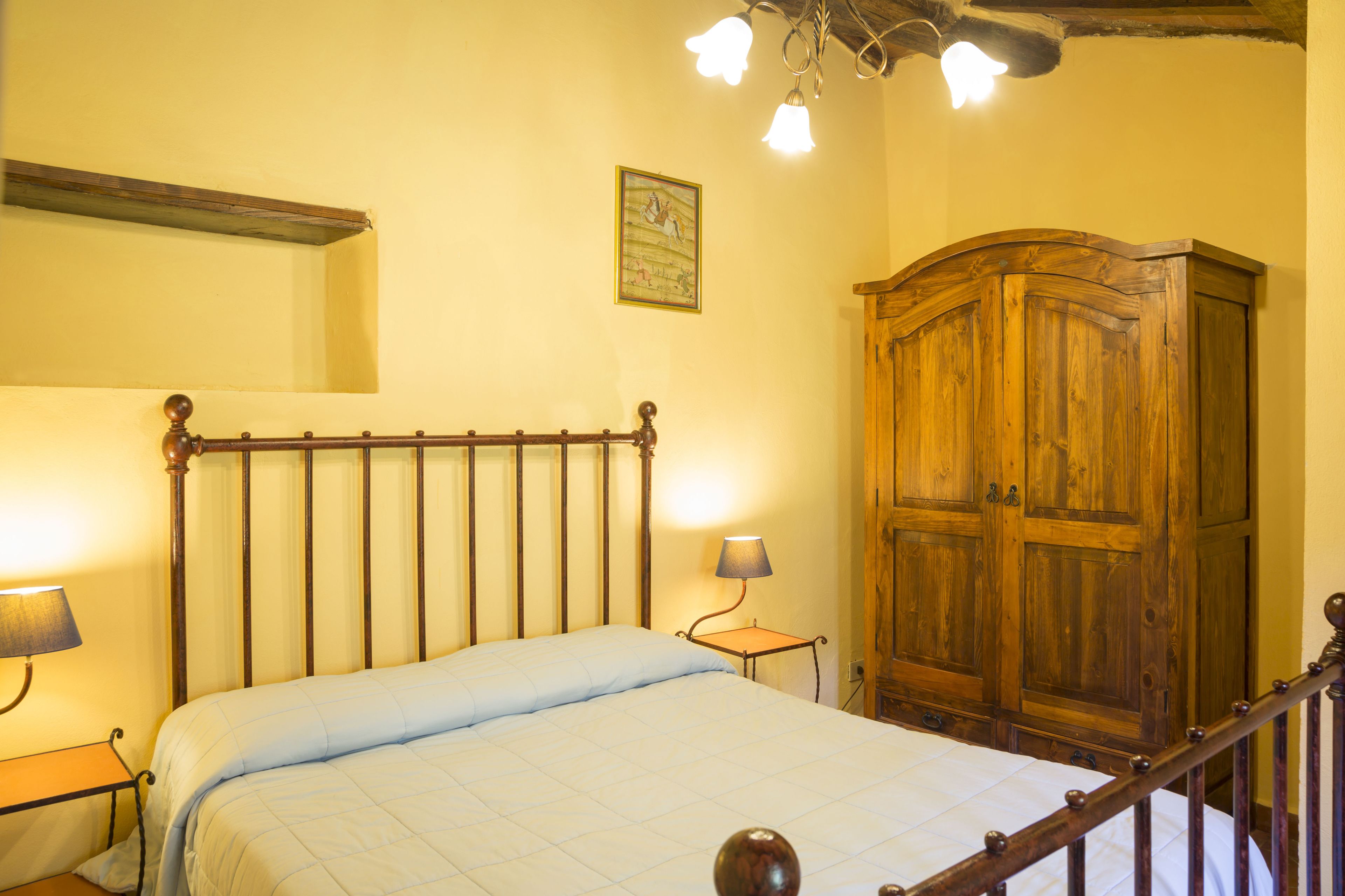 Une chambre à coucher avec un lit en bois, une table de chevet avec une lampe, une armoire et un luminaire au plafond.