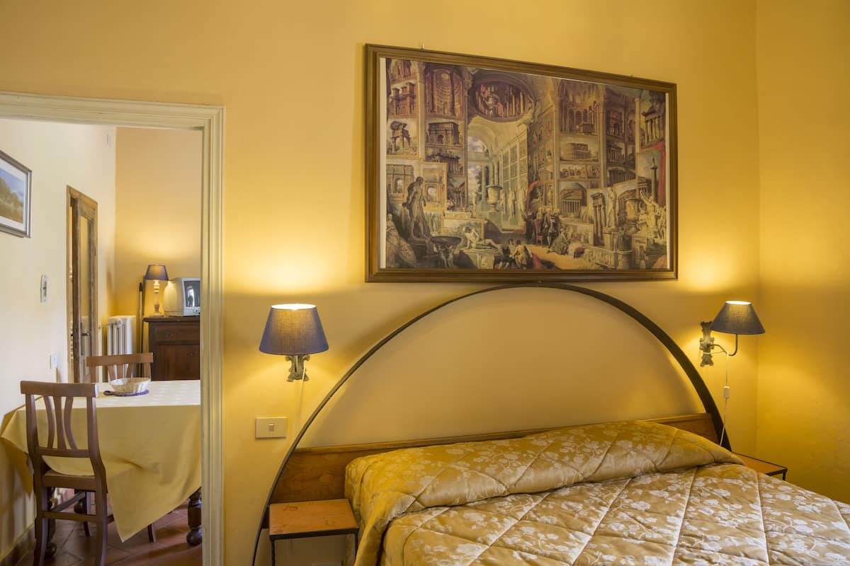 A hotel room with a bed, a dining table with chairs, and a wall-mounted painting.