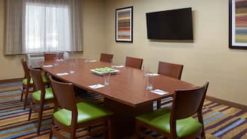 Een vergaderruimte met een grote houten tafel, groene bekleden stoelen en een kleurrijk gestreept tapijt.